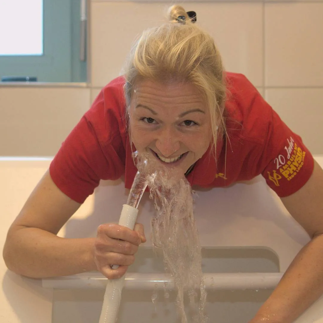 Mitarbeiterin im roten Poloshirt beugt sich über eine Wanne, aus einem Schlauch strömt Wasser