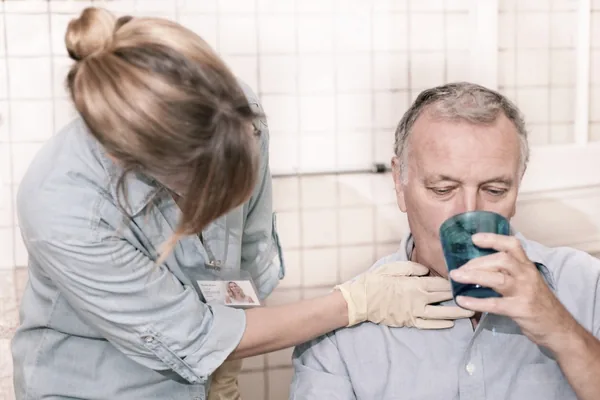 Therapeutin reicht einem älteren Patienten einen Becher und begleitet ihn beim Trinken