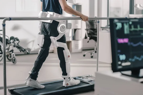 Patient geht im Exoskelett auf einem Laufband, daneben die Messbildschirme