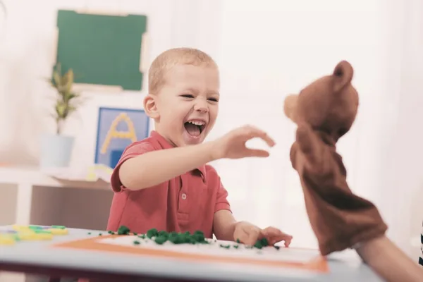 Kind lacht und greift nach einer Bären-Handpuppe, die ihm entgegengehalten wird