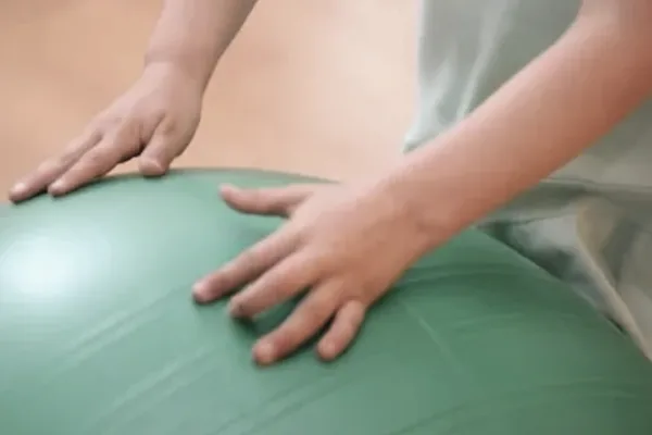 Zwei Hände stützen sich auf einem großen grünen Gymnastikball ab