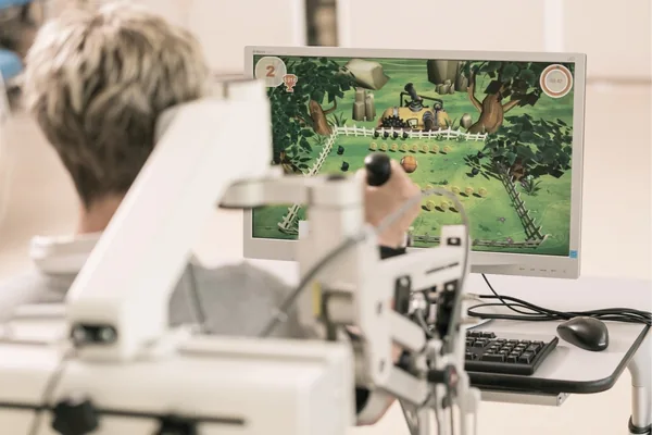 Patientin trainiert am RehaCom-Bildschirm, vor ihr ein Bediengerät mit Joystick