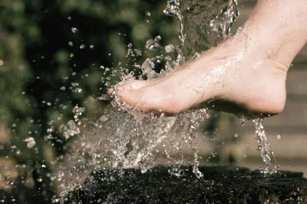Nackter Fuß tritt in aufspritzendes Wasser, im Hintergrund grüne Pflanzen